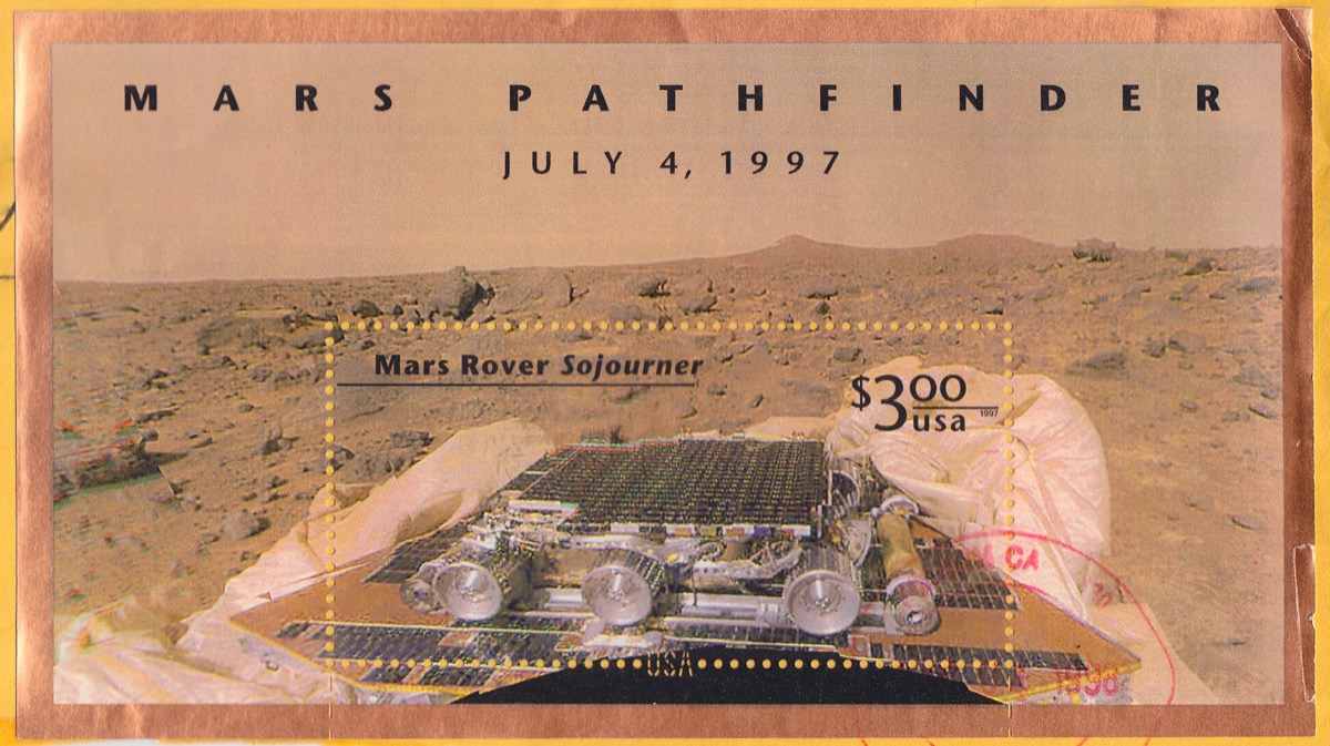 a colorized post stamp of the desert landscape of mars with a small rover on the platform of a lander. the post stamp reads "mars pathfinder july 4, 1997" and below "mars rover sojourner $3.00 USA"