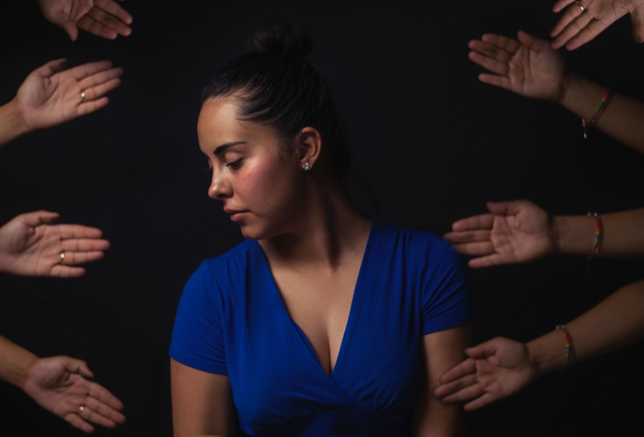 a woman with her eyes closed, head turned to the left. four pairs of hands are placed around her in an artistic fashion