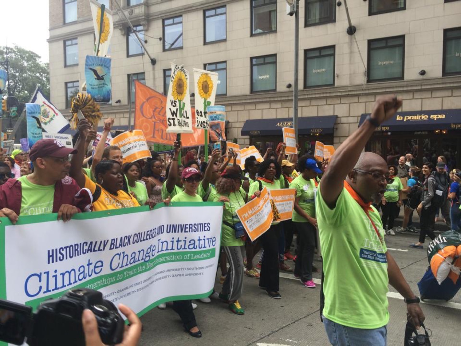 a group of black people coming together to march in a protest against climate change. their hands are raised in the air and they hold a banner that reads historically black colleges and universities climate change initiative