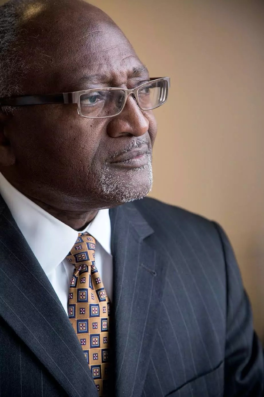 a profile headshot of a black man with glasses in a suit