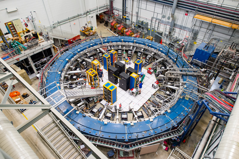 a look from above at a large blue circular lab equipment, the accelerator, in a warehouse-looking laboratory