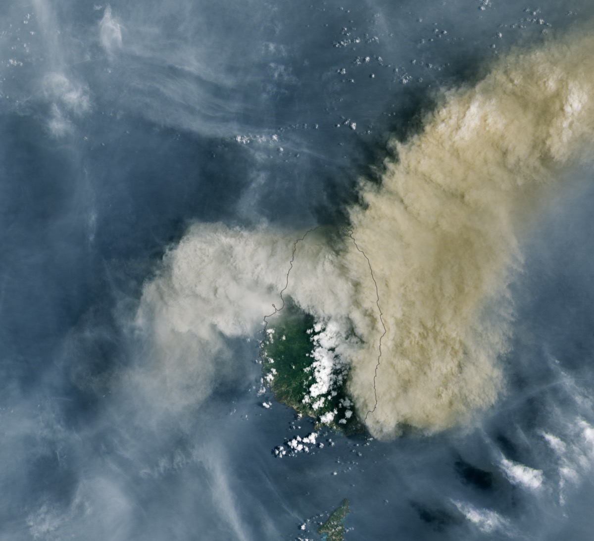 a satellite image of st vincent island, mostly shrouded by the plume of a volcano, drifting off to the right