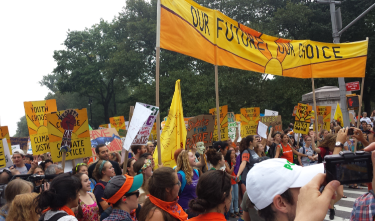 a large crowd of young people marching with yellow signs that read "our future, our choice"