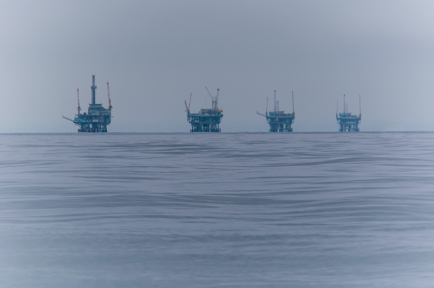 four oil rig platforms seen out in the misty distance on the horizon of the ocean