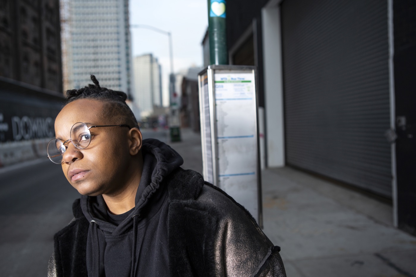 A transmasculine person waiting for the bus in a city close up