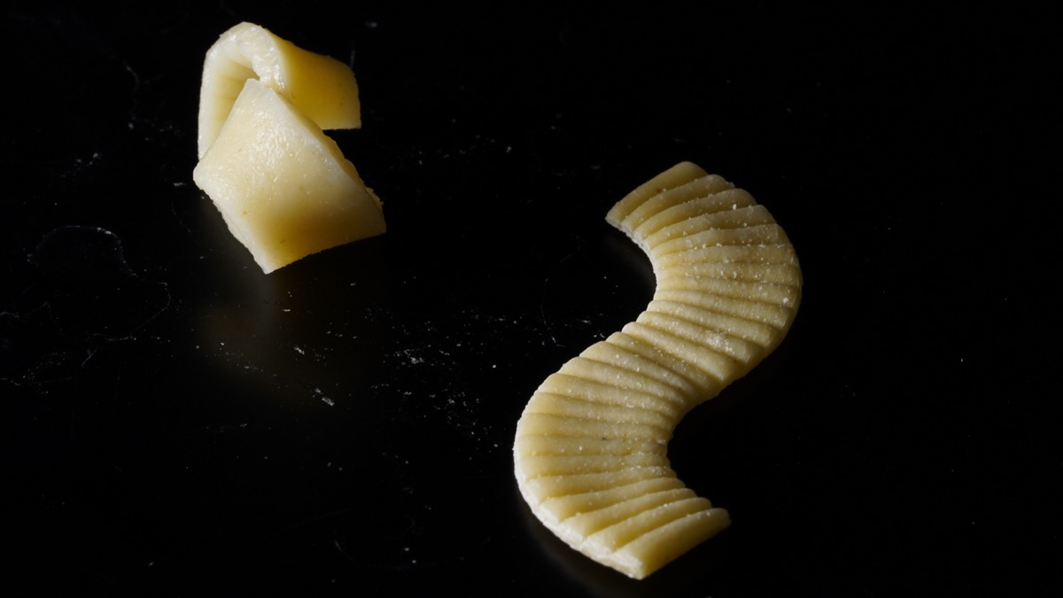 two pieces of pasta side by side. on the right is the pasta flat in a curved s-shape, on the left is that pasta after boiling in a curled up shape