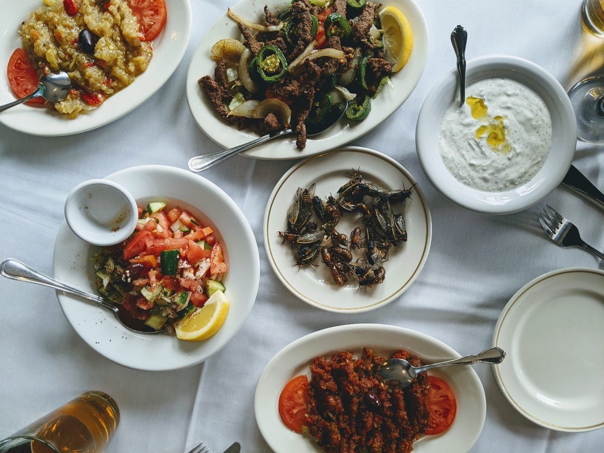 an above view of a dinner table with a white cloth and various dishes, including a plate of cicadas in the middle