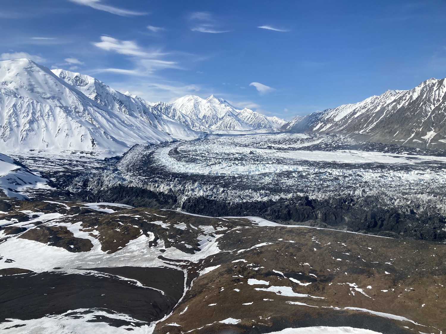 a mountainous landscape, half covered in snow, with a sweeping flat glacial body in the center at the foot of the mountains