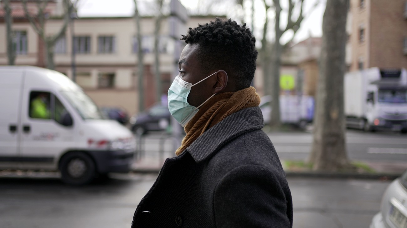 a black person wearing a mask on the street with cars and buildings behind them