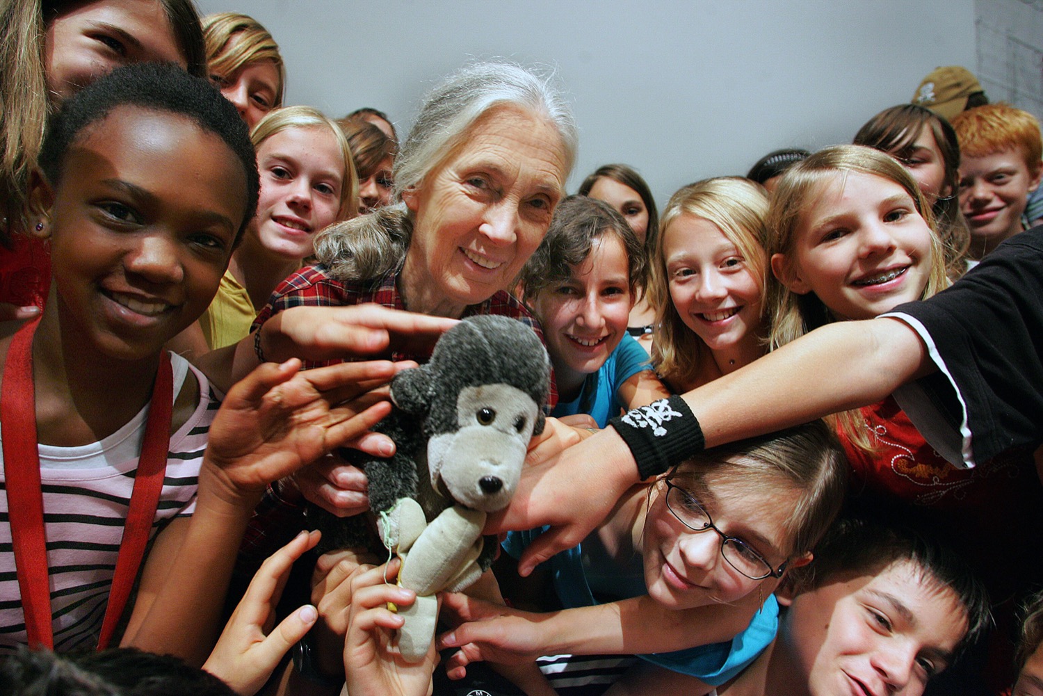 an older woman holds a stuffed monkey and is surrounded by smiling children