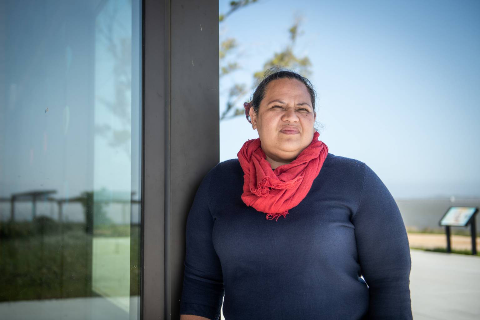 a samoan woman in a red scarf and navy shirt leaning against a glass door