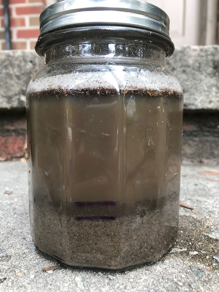Jar of muddy water and soil after a shake test. First two layers are marked to indicate level of sand and silt particles.