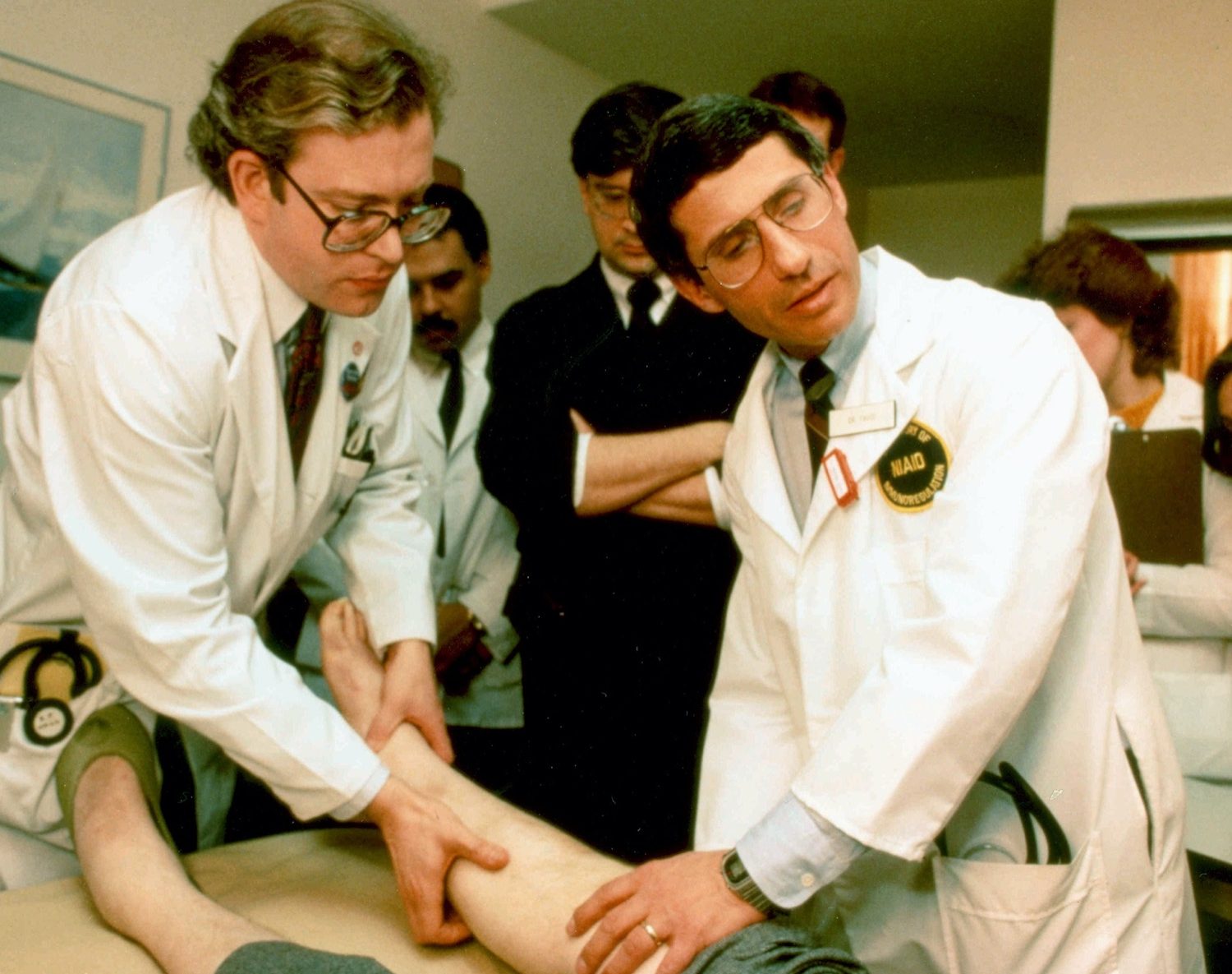 two male doctors in lab coats lift up a patients leg in an examine