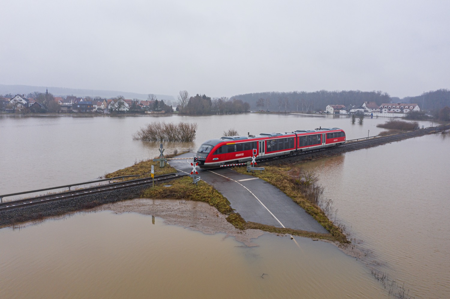 a small train passes over a flooded landscape, with a road partially submerged