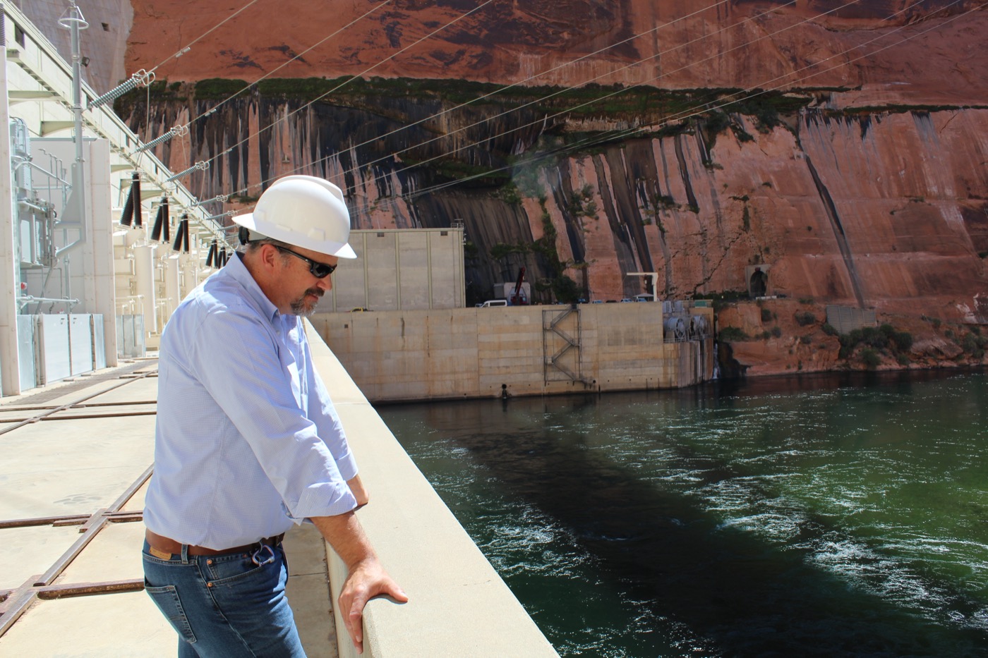 a white man in a hard hat looks over the edge of a dam