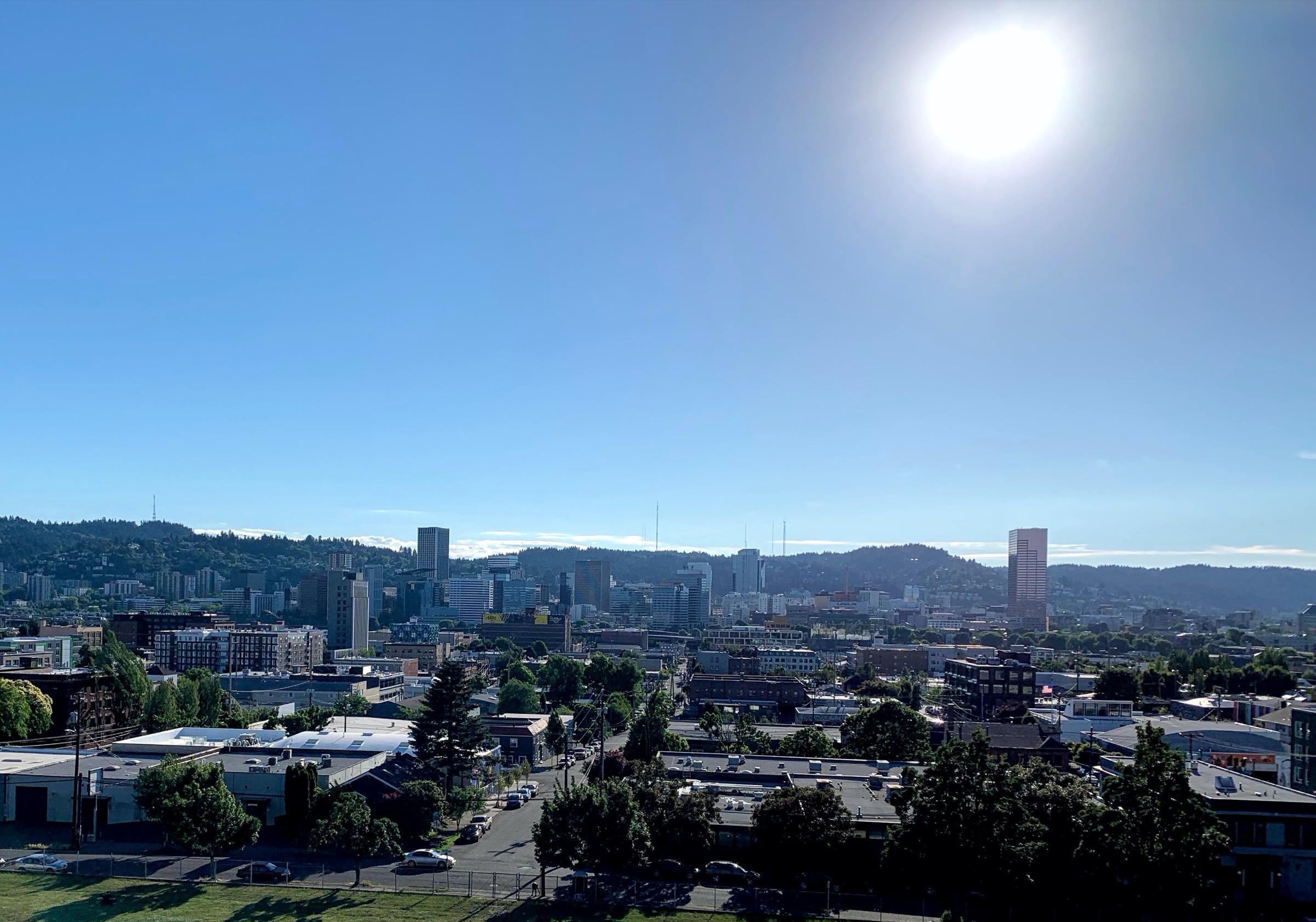 a clear hot day looking at downtown portland with mountains in the distance with the sun in frame