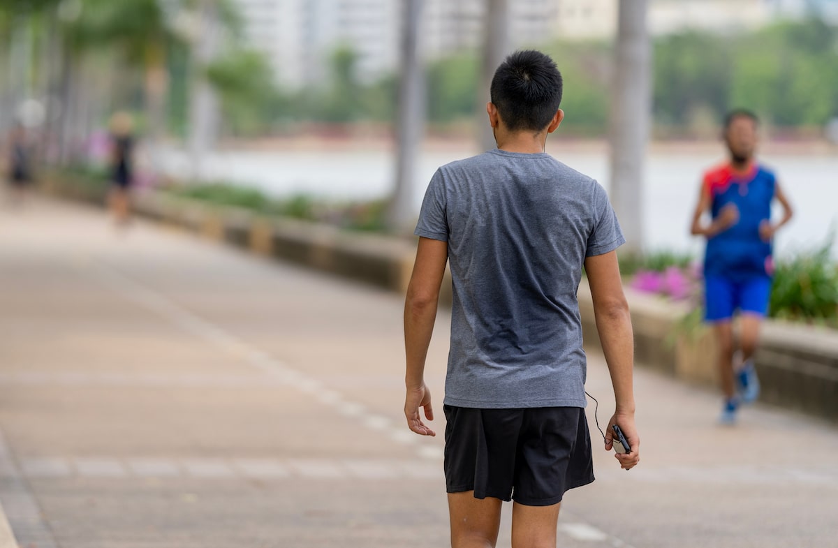 The back view of a man wearing a gray T-shirt is exercising hard, causing his back to be sweaty in the park.