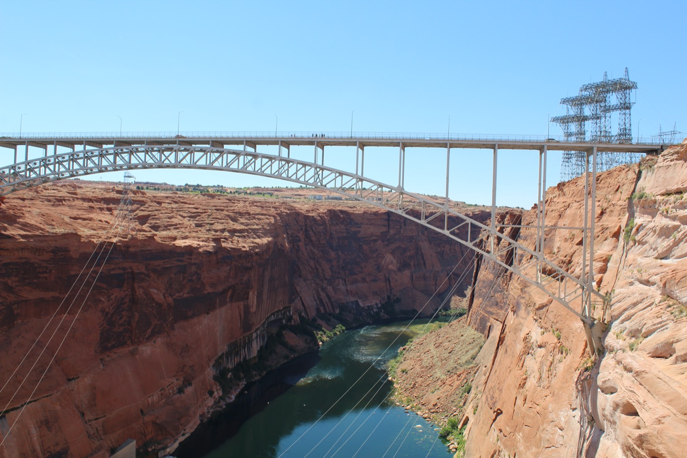 a landscape shot of a gap between a canyon with water running beneath it. a bridge and power lines span the gap