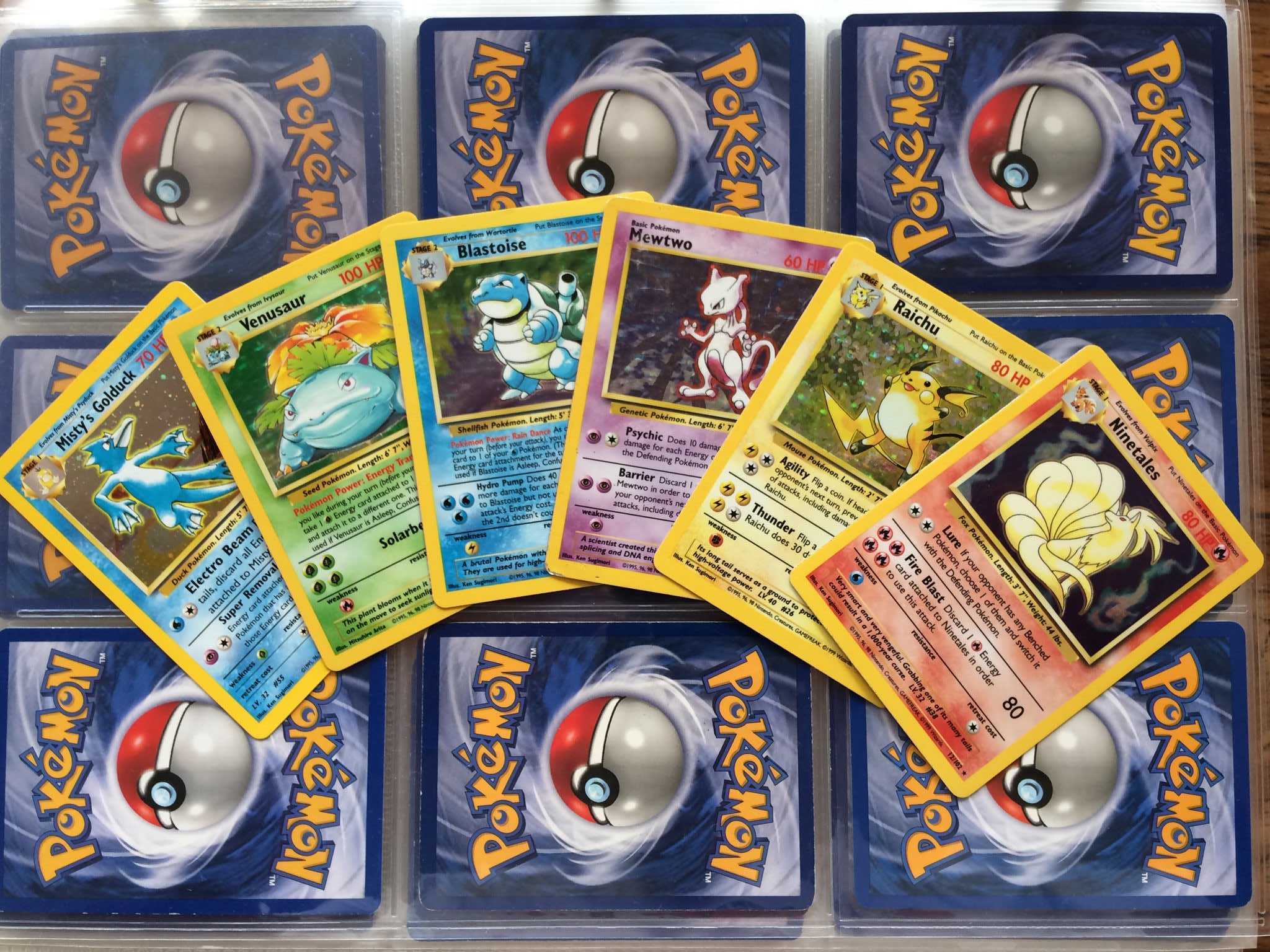 six holographic colorful pokemon trading cards, including golduck, venusaur, blastoise, mewtwo, raichu, ninetails, fanned out over a binder sheet of pokemon cards