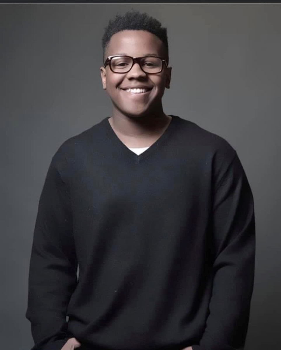 a smiling young black man with glasses and a black sweater