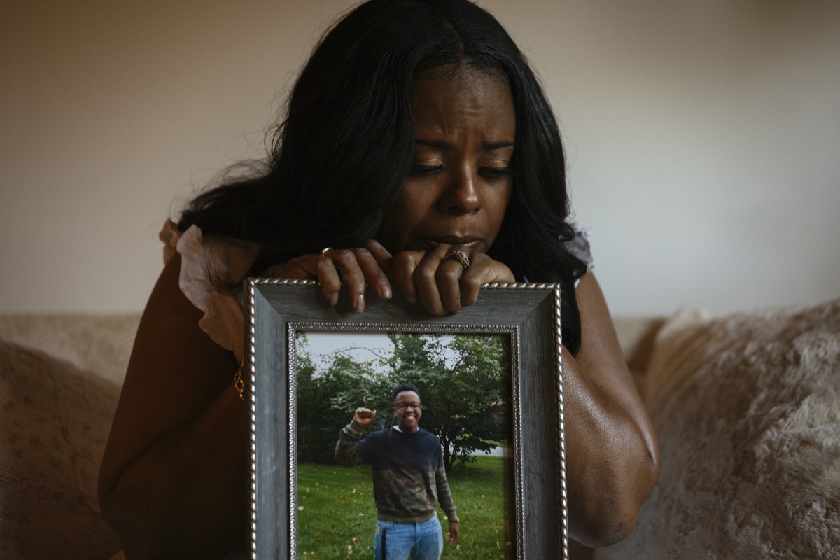 a black woman sadly holding a framed portrait of her son