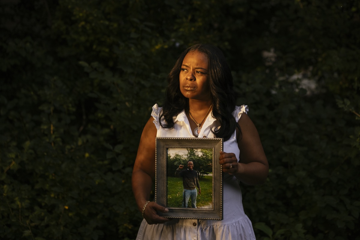 a black woman standing outside with the soft sunlight casting over her face as she holds a portrait of her son