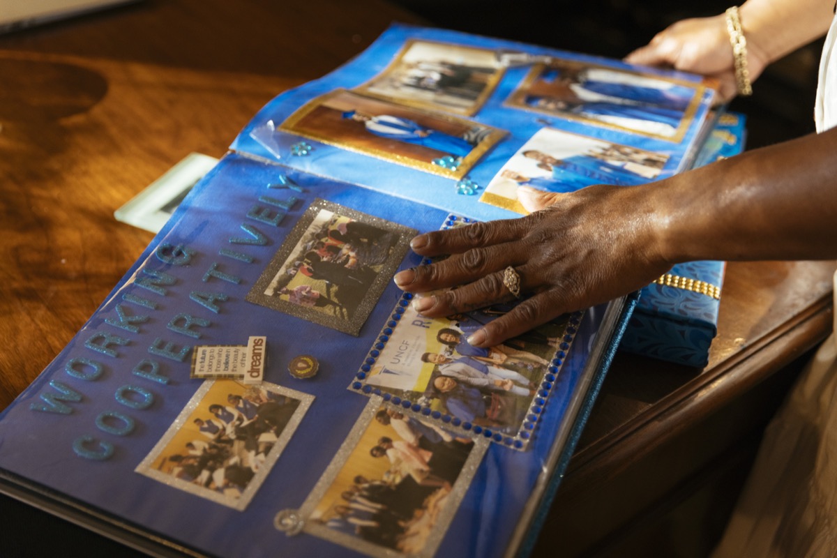 the hand of a black woman pages through a scrap book filled with photos of her son's life