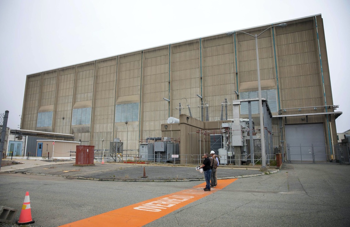 a brown building with a few people with hard hats standing on a bright orange line outside looking out at the facility