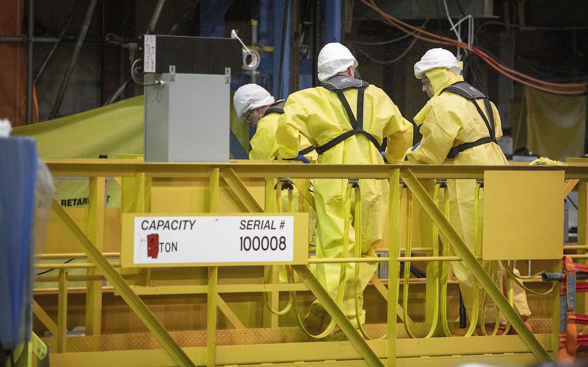a crew in yellow hazmat suits and white hard hats work on a yellow lift