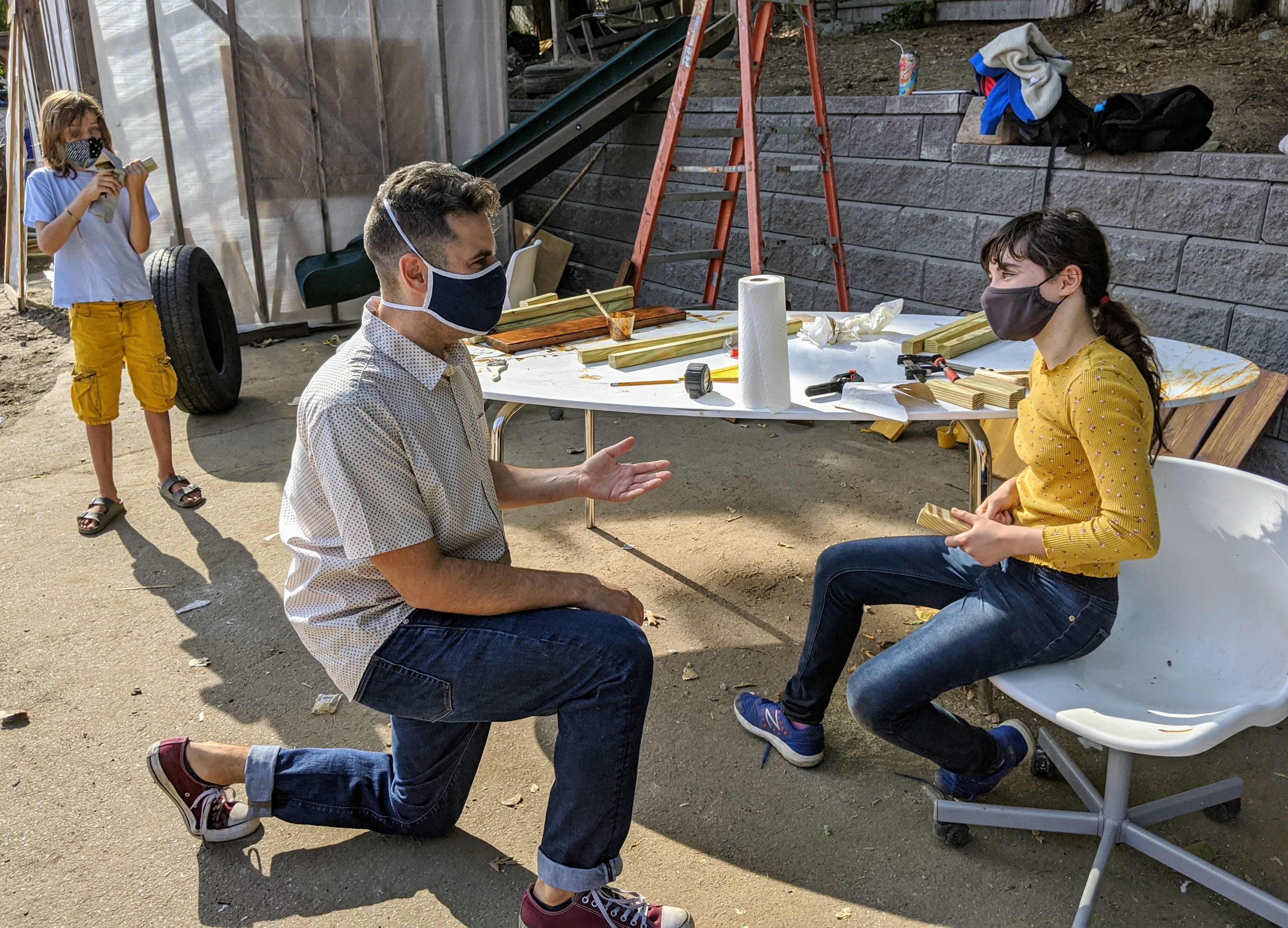 Educator Michael Hirsch kneeling in front of a student having a discussion. Students and teacher are wearing masks