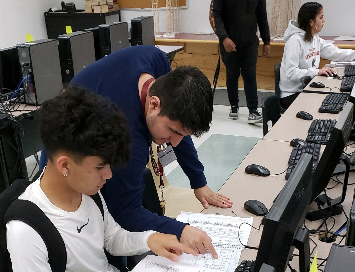 Educator Sergio Estrada and student looking at data on a paper. Two students in background.