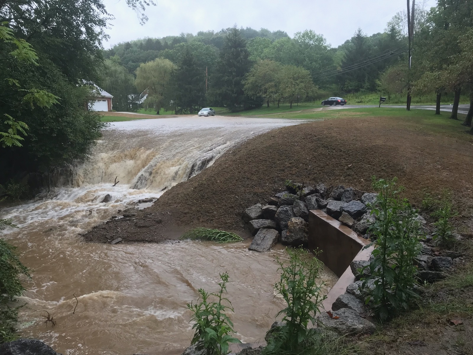 a waterfall of flooding going over a hill on a quiet residential street