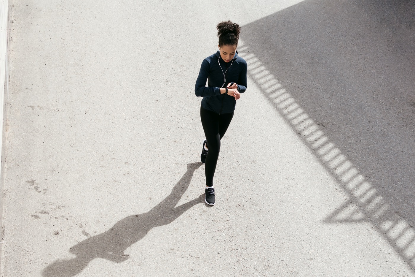 black woman walking outside in fitness clothing while checking her fitness tracker. its shot from above her