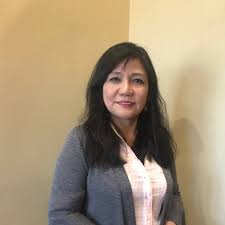 A Filipina nurse in a blazer stands against a yellow wall