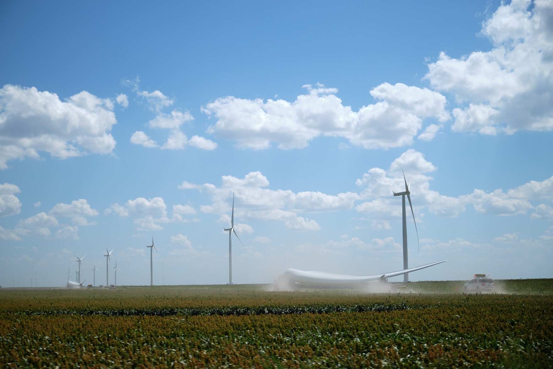 a landscape shot of a large farm field with seven wind turbines dotting the landscape. one turbine blade lies on the ground
