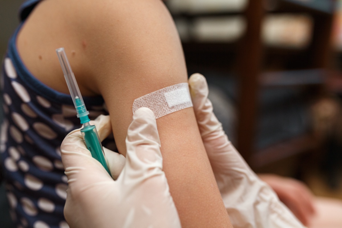 a child's arm with a clinician putting a band aid on it, also holding a syringe