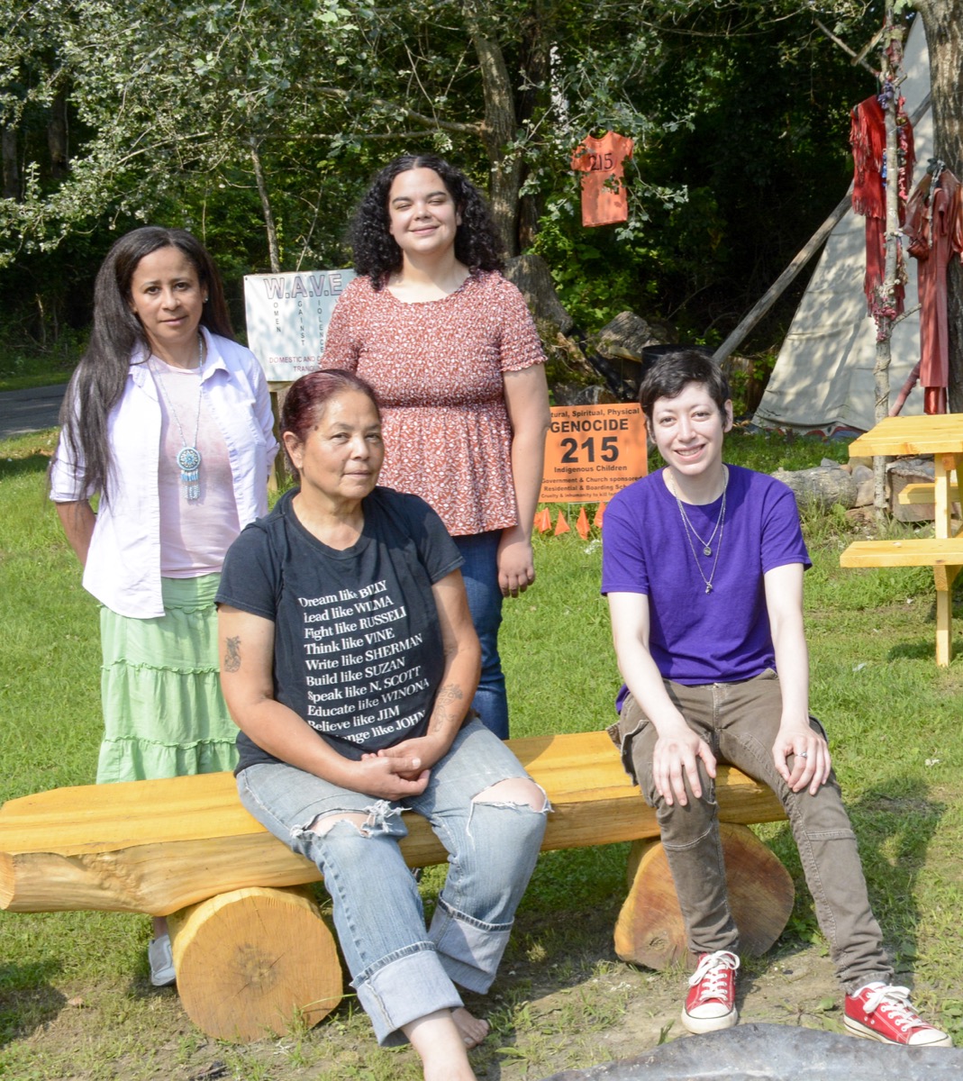 our members of the shinnecock tribe sit on a bench outside smiling. 