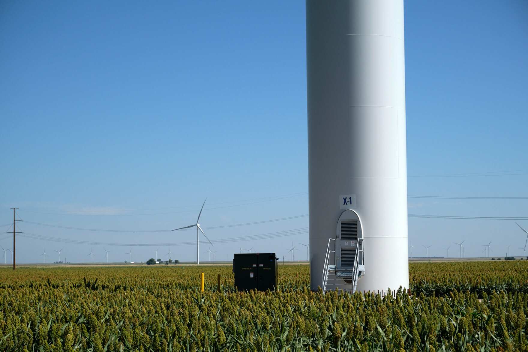 the base of one of the wind towers in a field. a small staircase leads up to a door in the base of the turbine