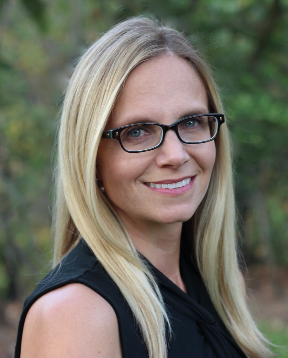 a headshot of a blonde woman with black rimmed glasses