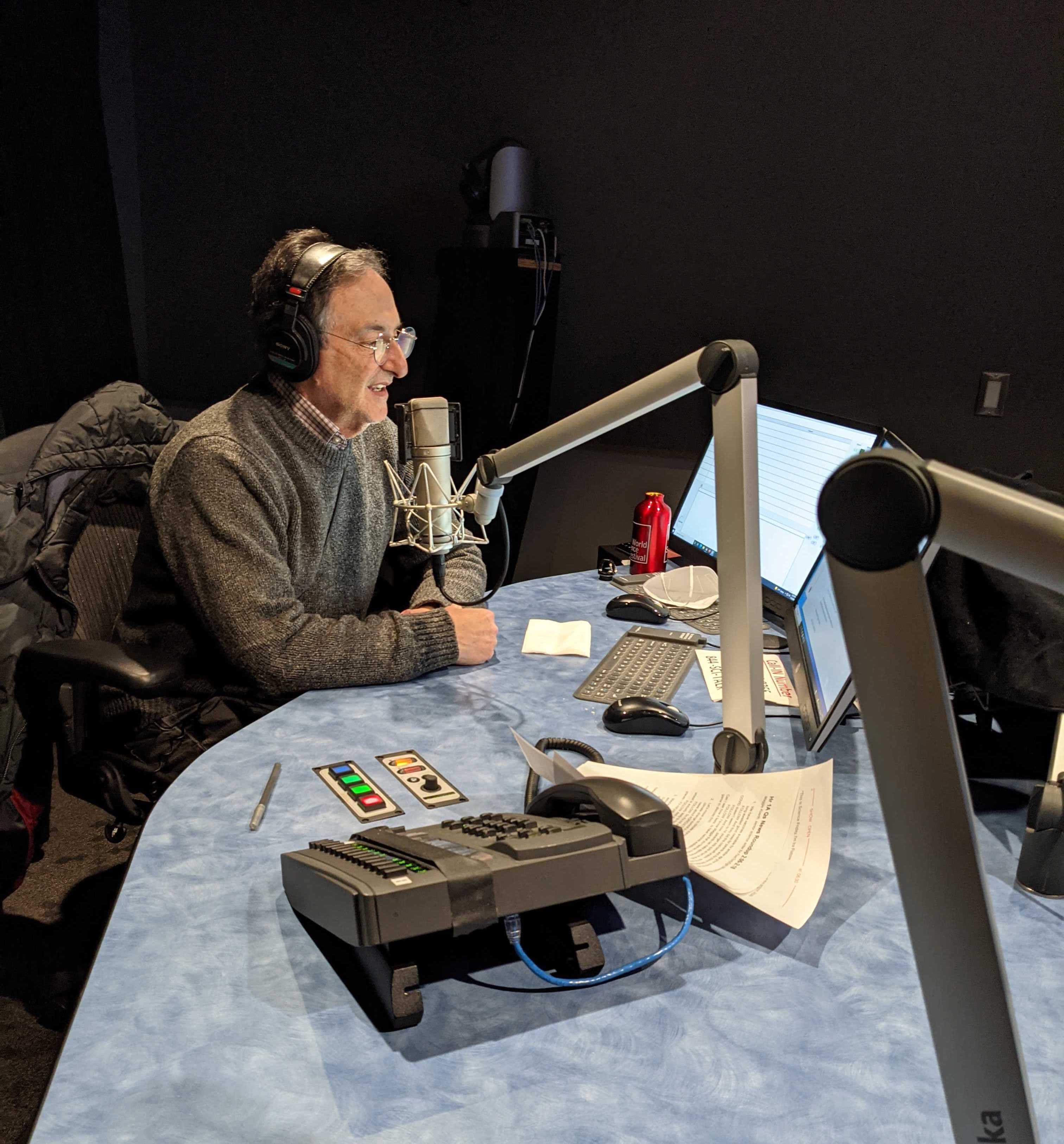 a man wearing glasses and headphones speaks into a microphone in a radio studio