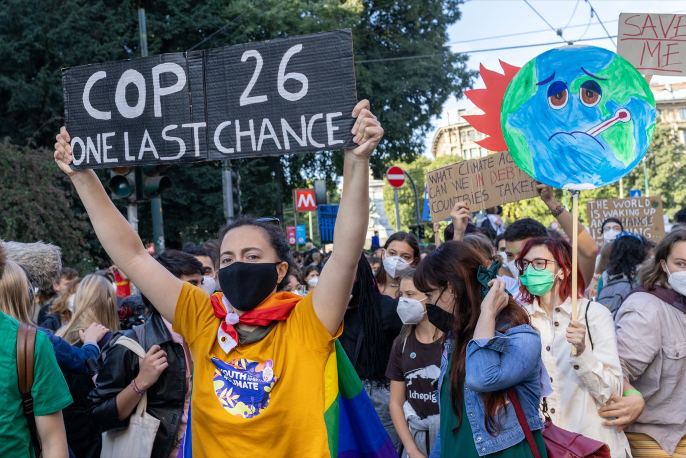 dozens of young people wearing masks hold up signs including one that says "cop 26 one last chance" and one that's a cardboard circle illustration of an earth with a frowny face with a thermometer hanging out of its mouth