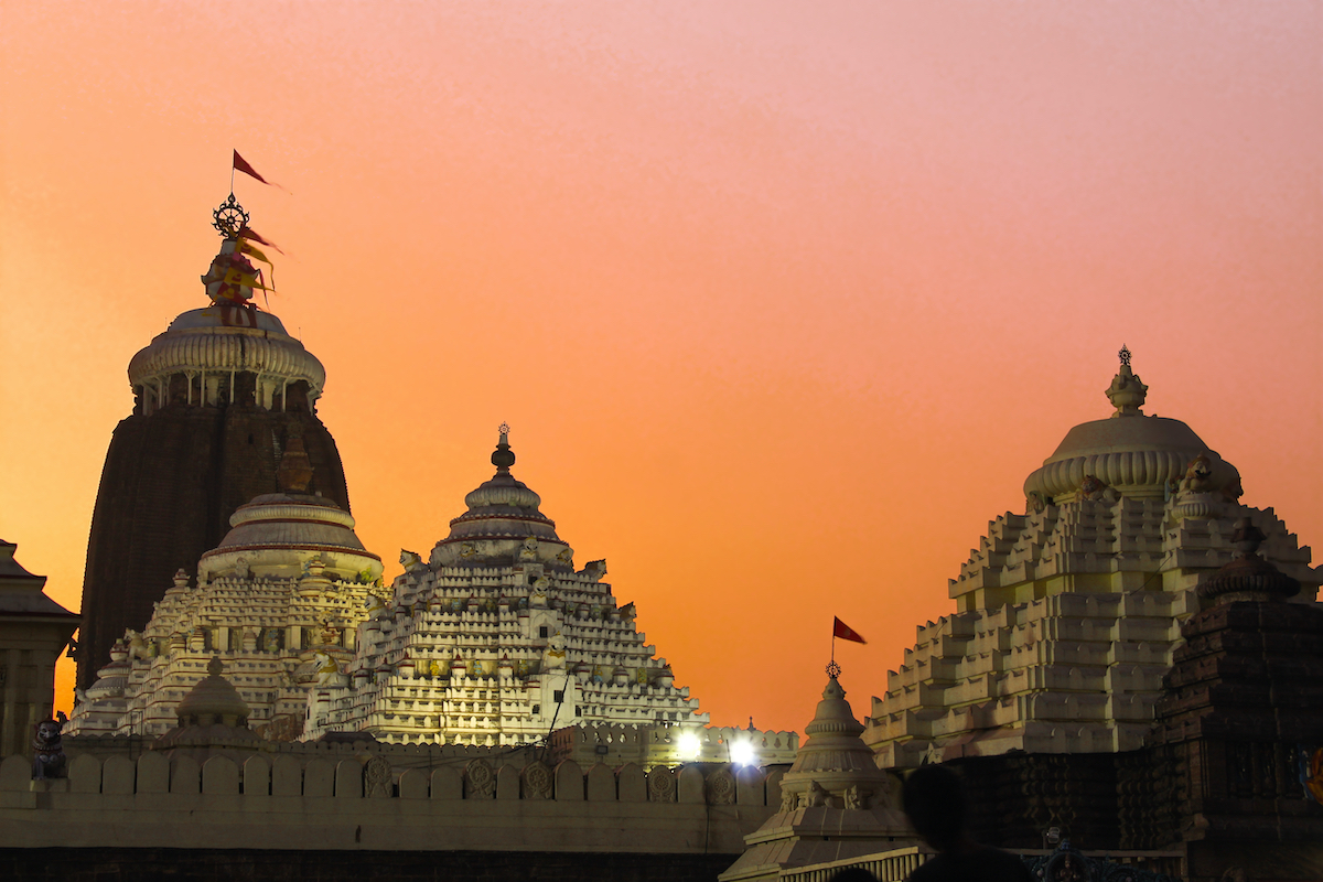 pyramid-like set of three temples - one with a flag flying int the breeze above - against a pinkish sunset