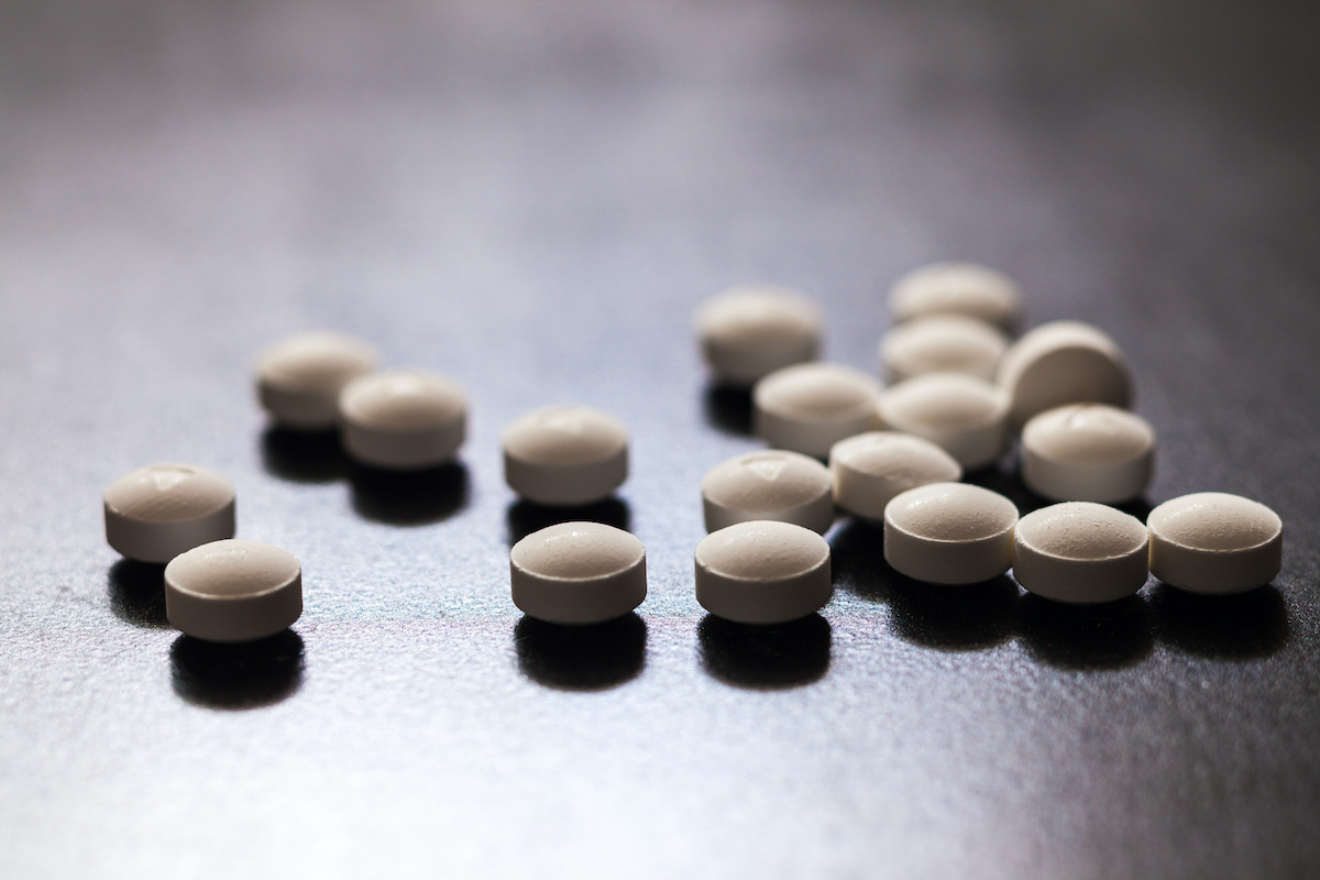 backlit white round opioid pills lying scattershot on a table