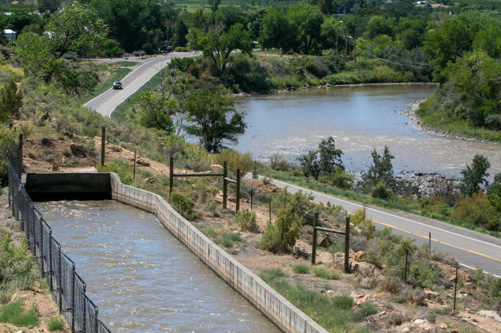 a landscape shot of a river on the left, a road to its left, and a sectioned off small irrigation canal to the left of the road