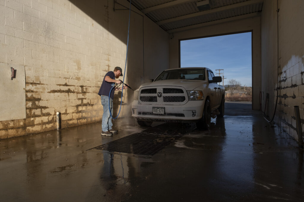 a white man hoses his truck down at a self service washing station