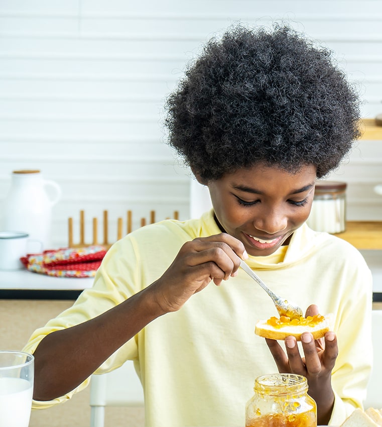 Kid spreading orange jam on toast.