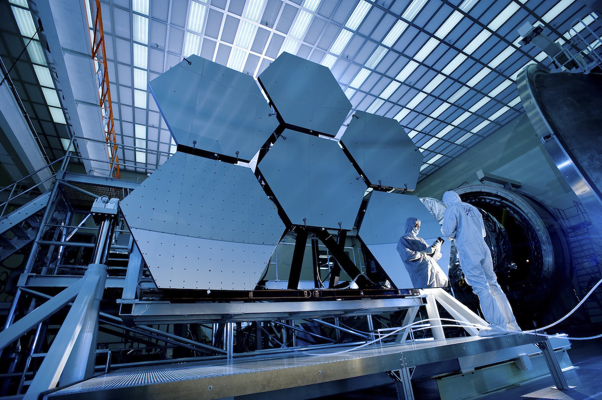 shot of six giant hexagonal mirrors with a scientist in a white jumpsuit reflected in one of the mirrors