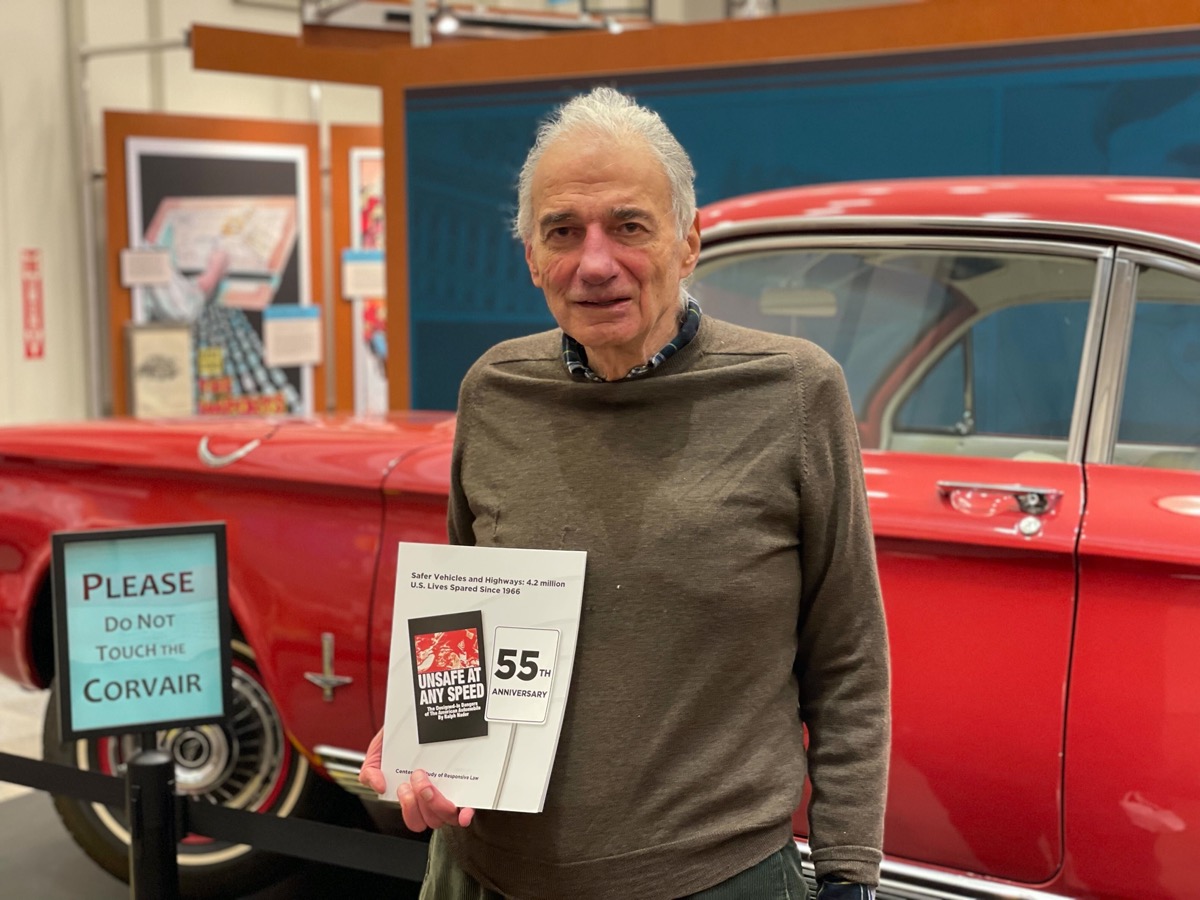 an older man holding a pamphlet in front of an older red car