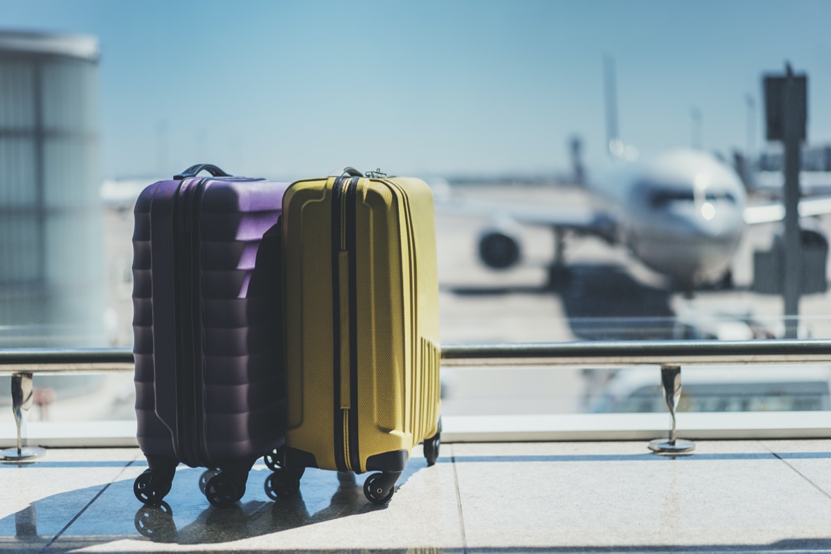 a purple and yellow roller suitcase in an airport with an airplane in the background