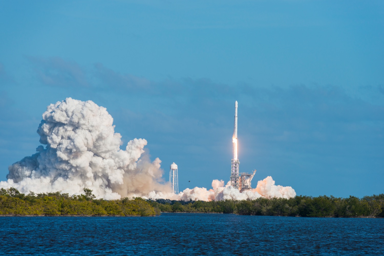 a rocket launching on a bright sunny day, with a marsh in the foreground